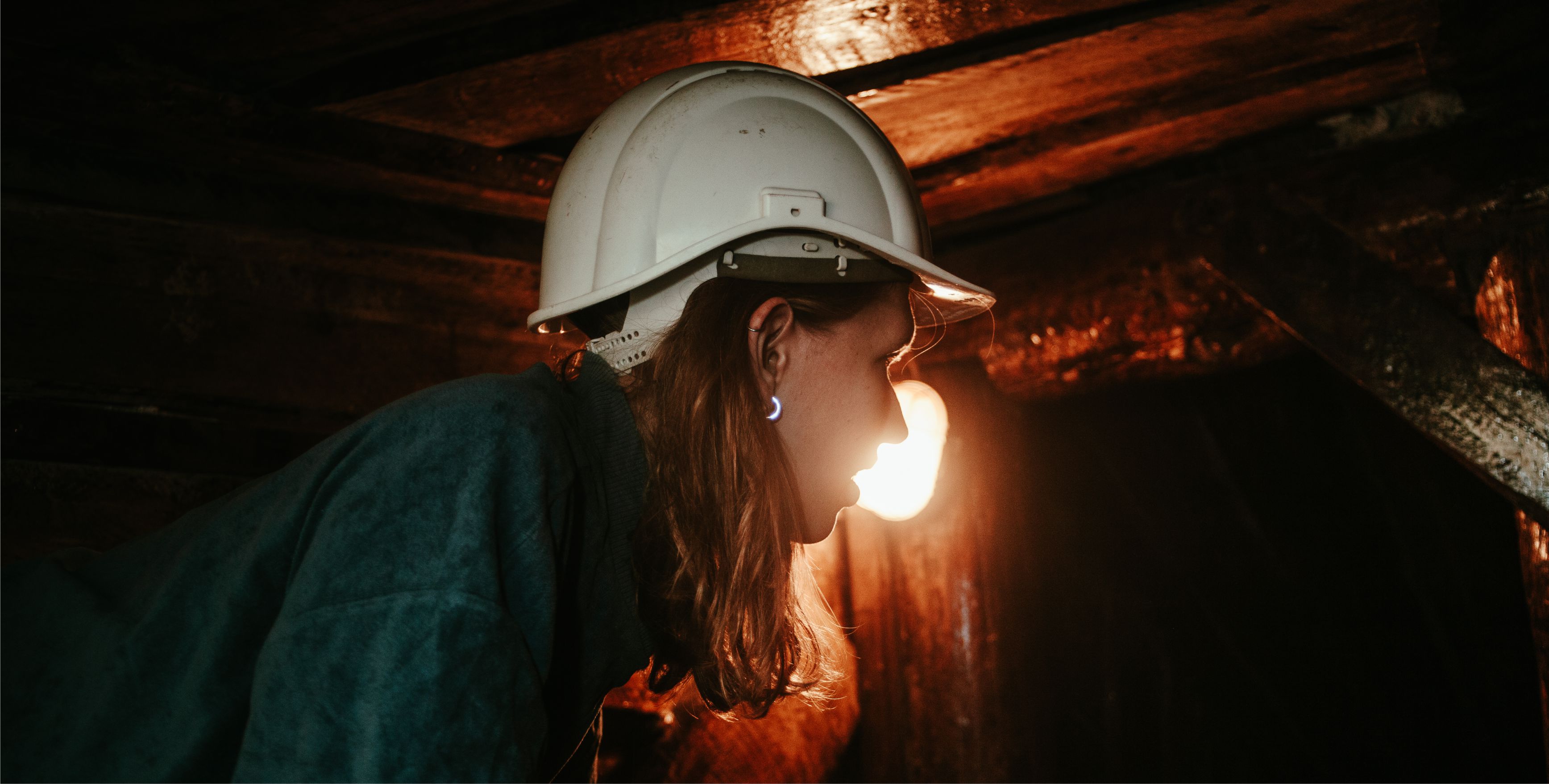 Junge Frau mit Helm im Halbportrt kriecht durch einen Bergwerksstollen
