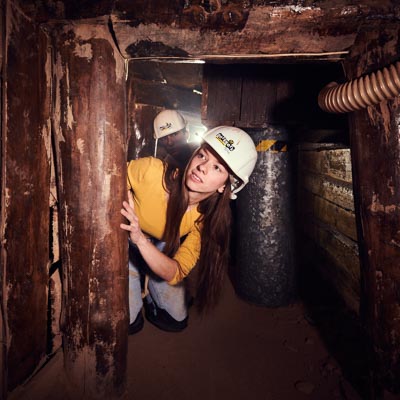 Junge Frau mit Helm sucht einen Weg durch einen Bergwerksstollen