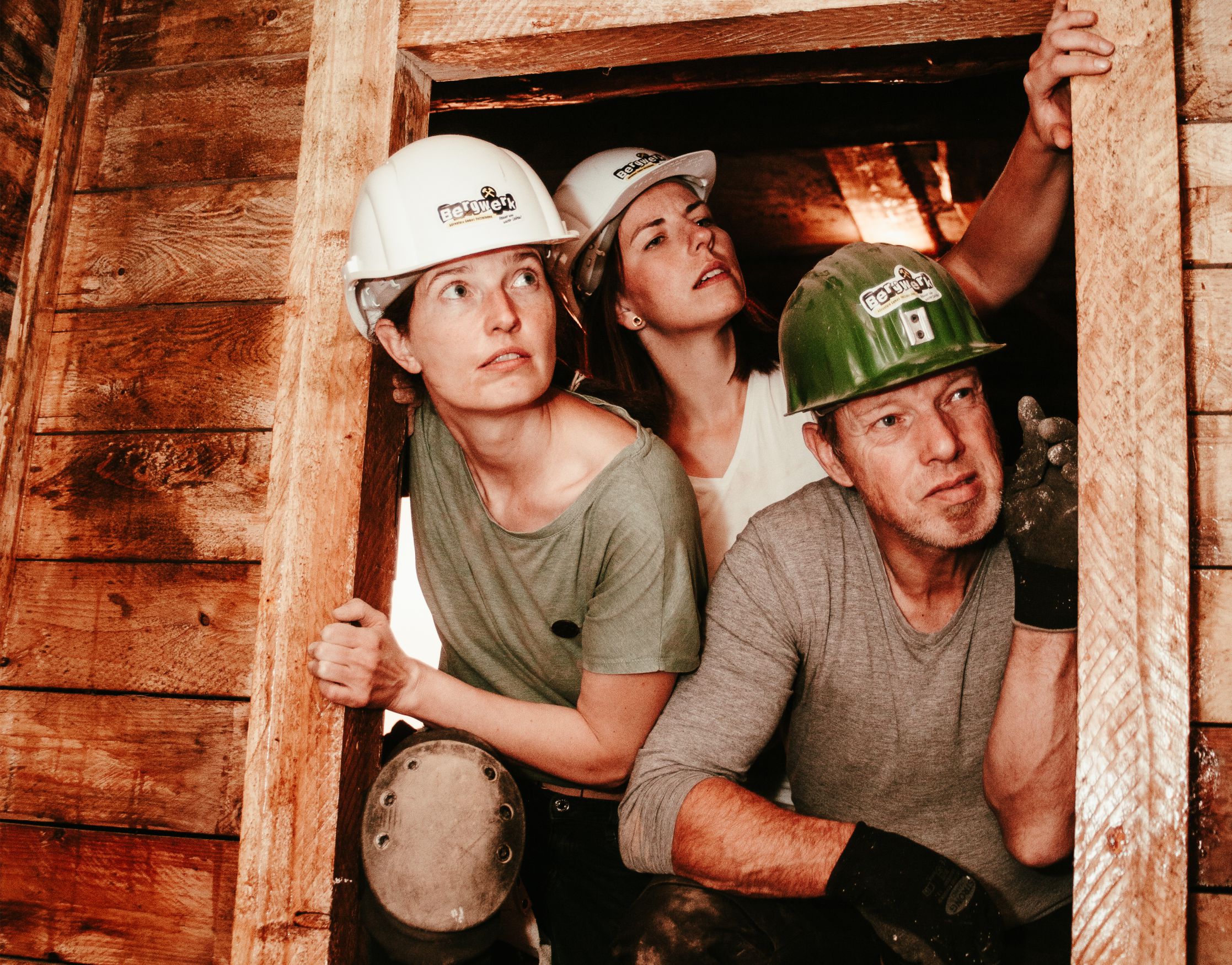 Drei Besucher mit Helmen blicken im Bergwerk aus einem Stollen