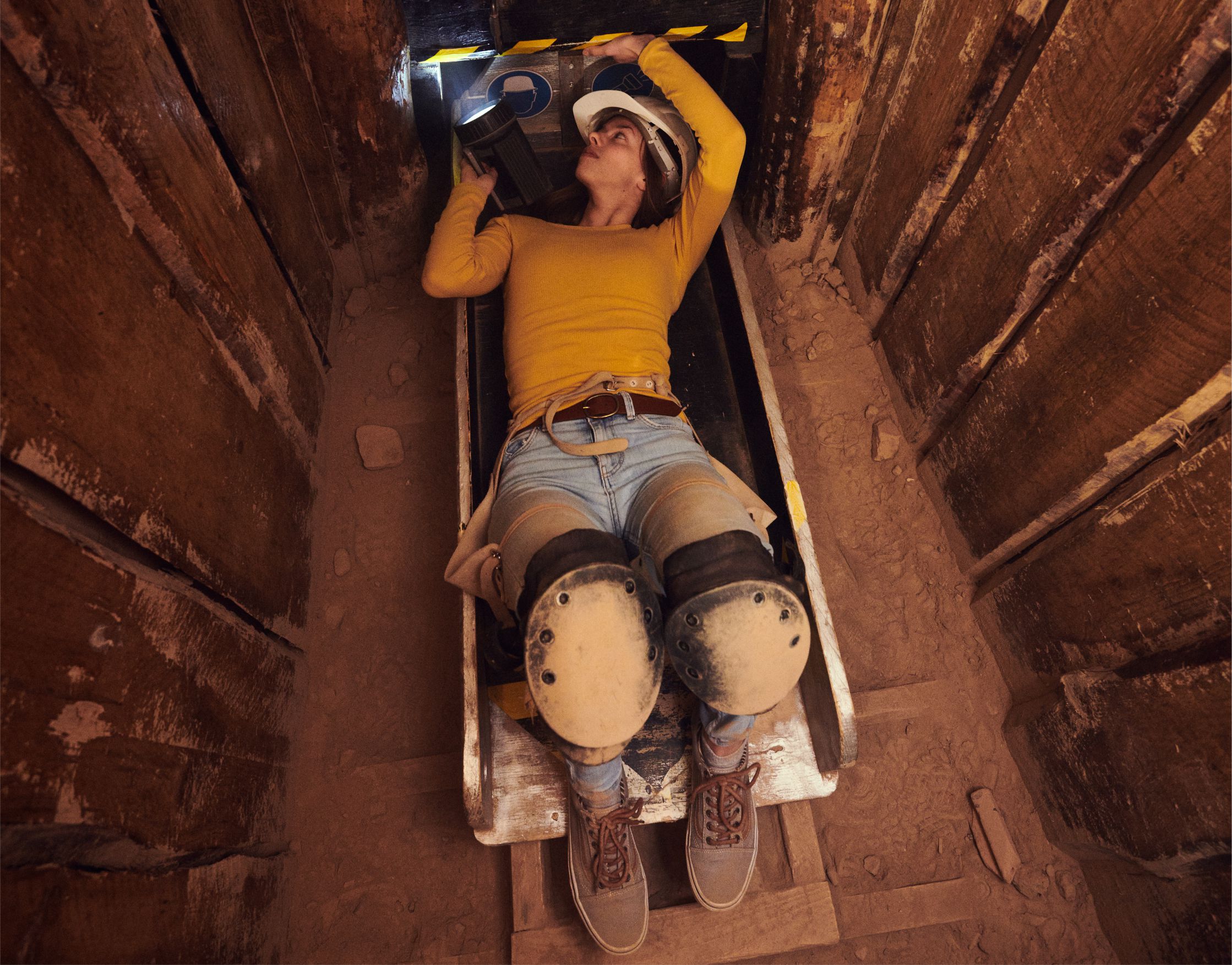 Junge Frau liegt auf dem Rcken und erkundet mit einer Lampe einen engen befahrbaren Schacht