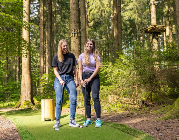zwei junge Frauen beim Adventure Golf spielen unterhalb des Kletterparks