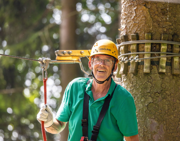 lterer Mann auf Kletterplattform vor einem Baum in Kletterpark