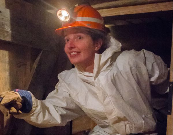 Junge Frau mit Helm und Stirnlampe erkundet Bergwerksstollen